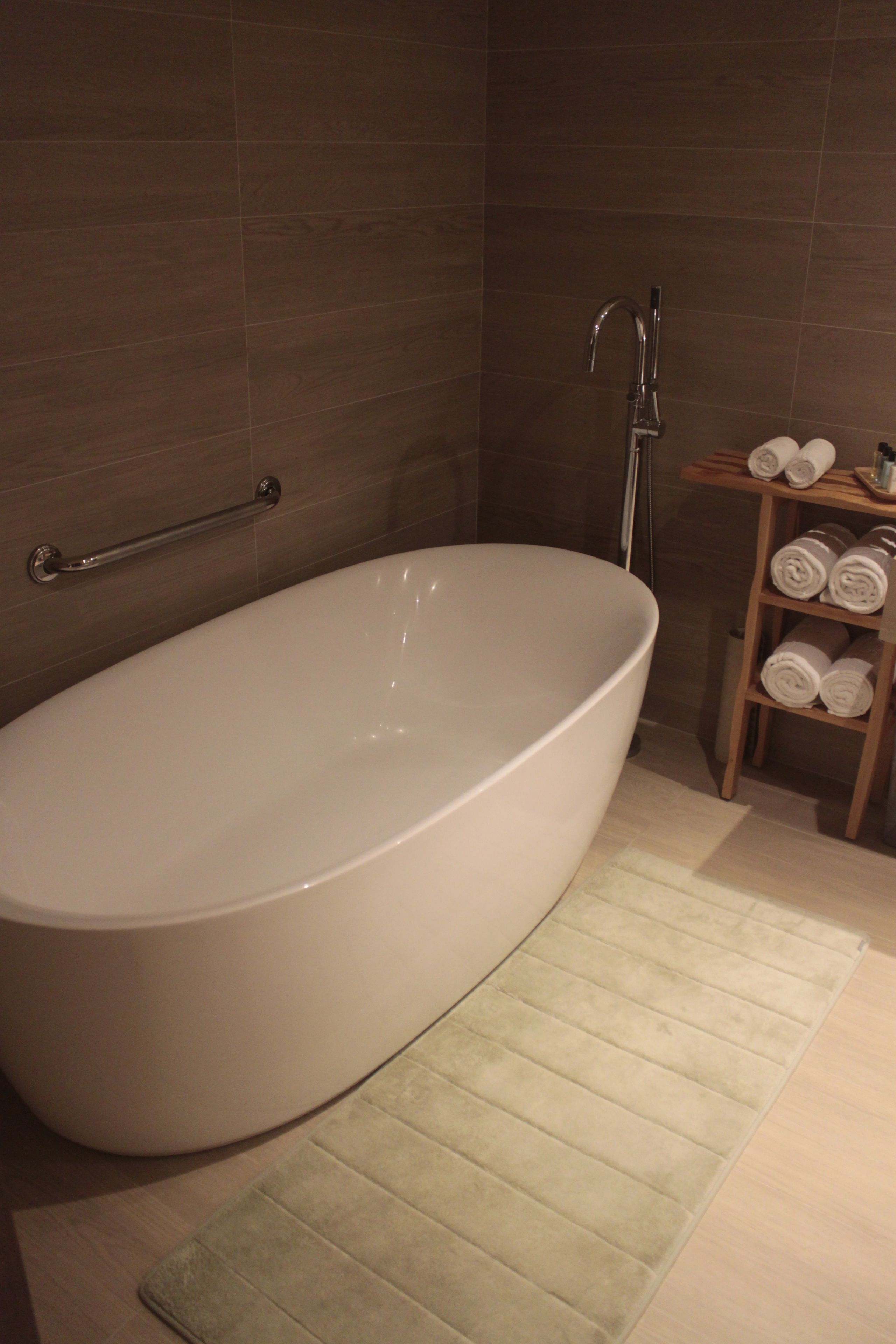 A modern bathroom with a freestanding bathtub, a towel rack, and a wooden shelf with towels.