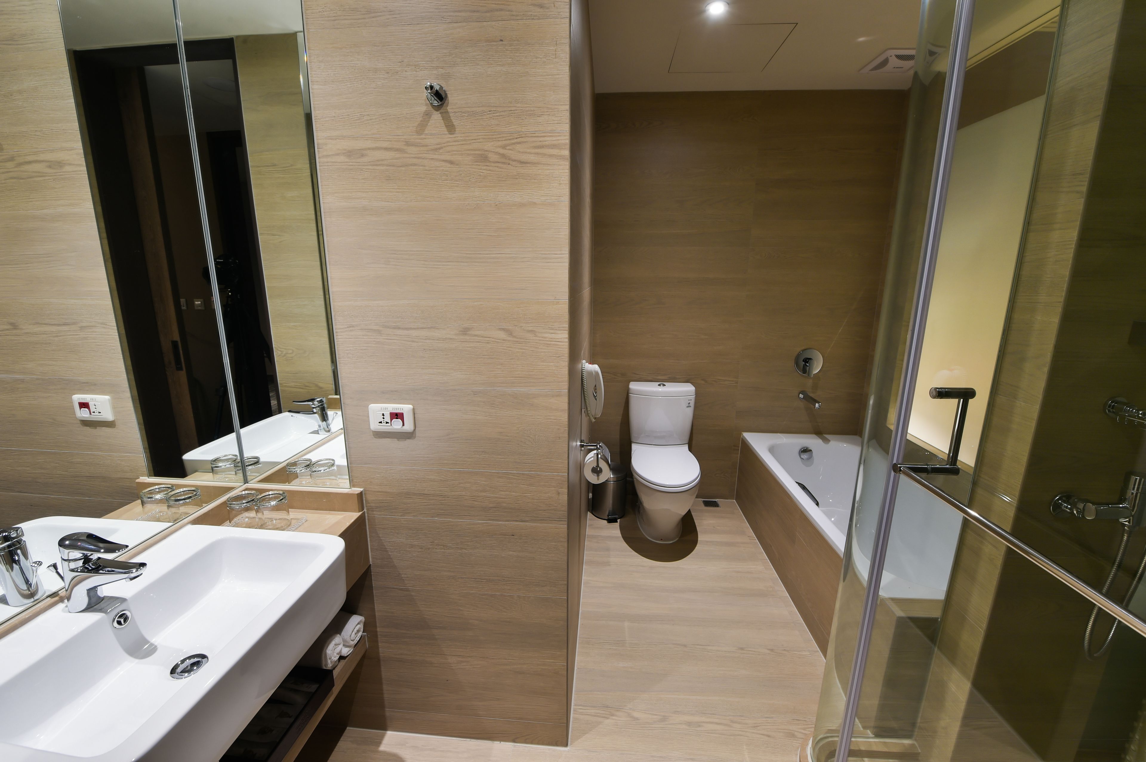 A modern bathroom with a large mirror, a sink, a toilet, and a bathtub.