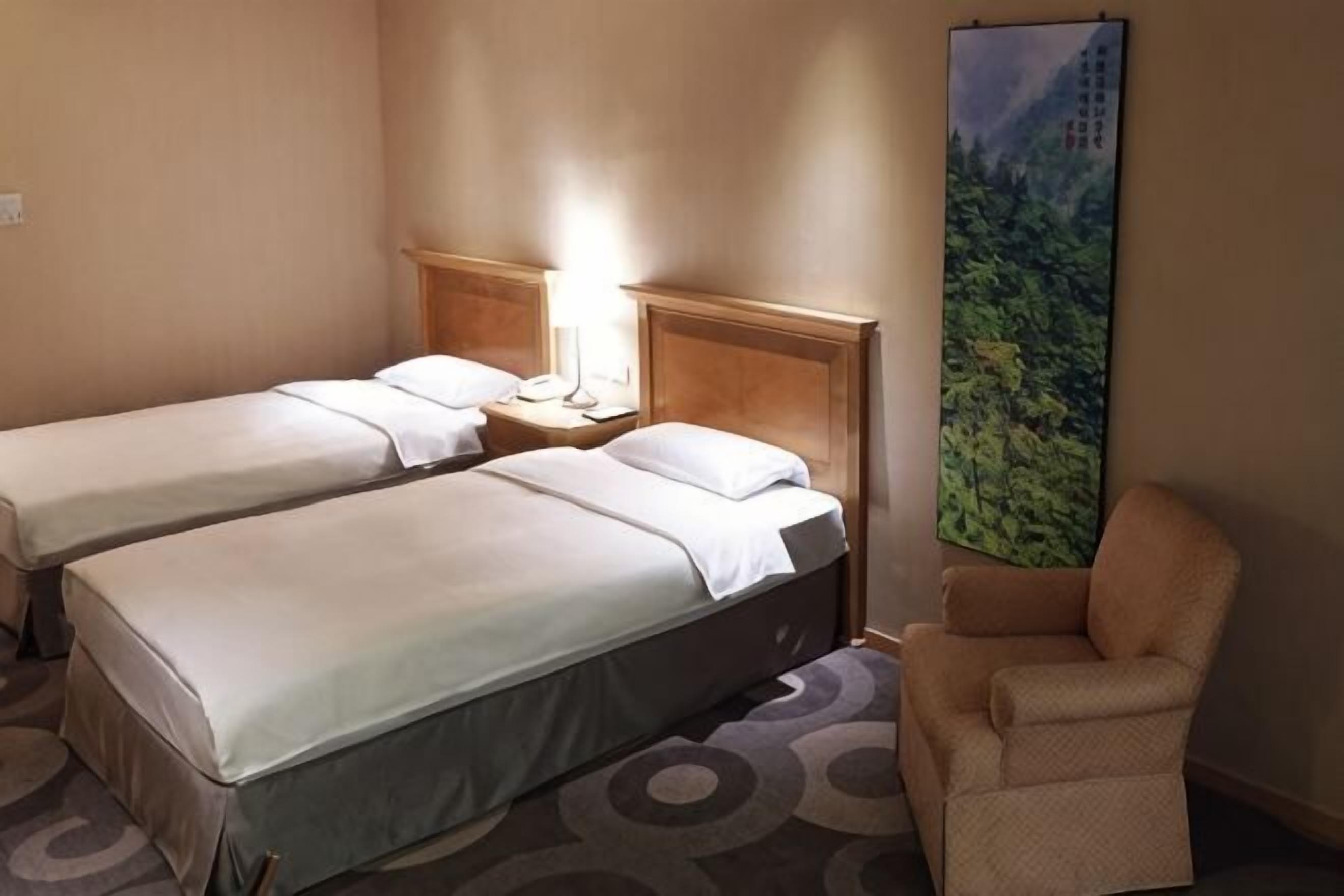 A hotel room with two beds, a chair, a nightstand, and a large painting.