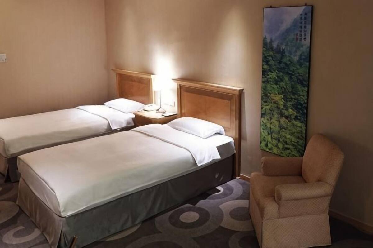 A hotel room with two beds, a chair, a nightstand, and a large painting.