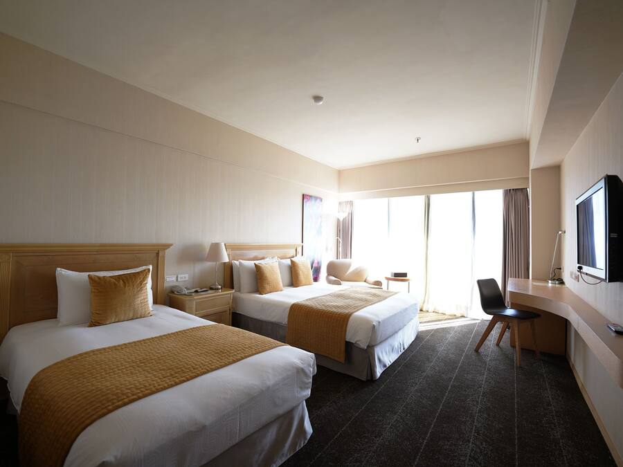 A hotel room with two beds, a desk, a chair, a television, and a large window with curtains.