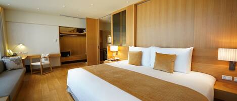A hotel room with a large bed, wooden headboard, bedside tables with lamps, a desk, and a wardrobe.