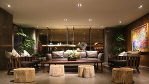 A modern lounge area with a sofa set, round wooden stools, and hanging pendant lights. - Maison de Chine Hotel Chiayi (Chiayi City)