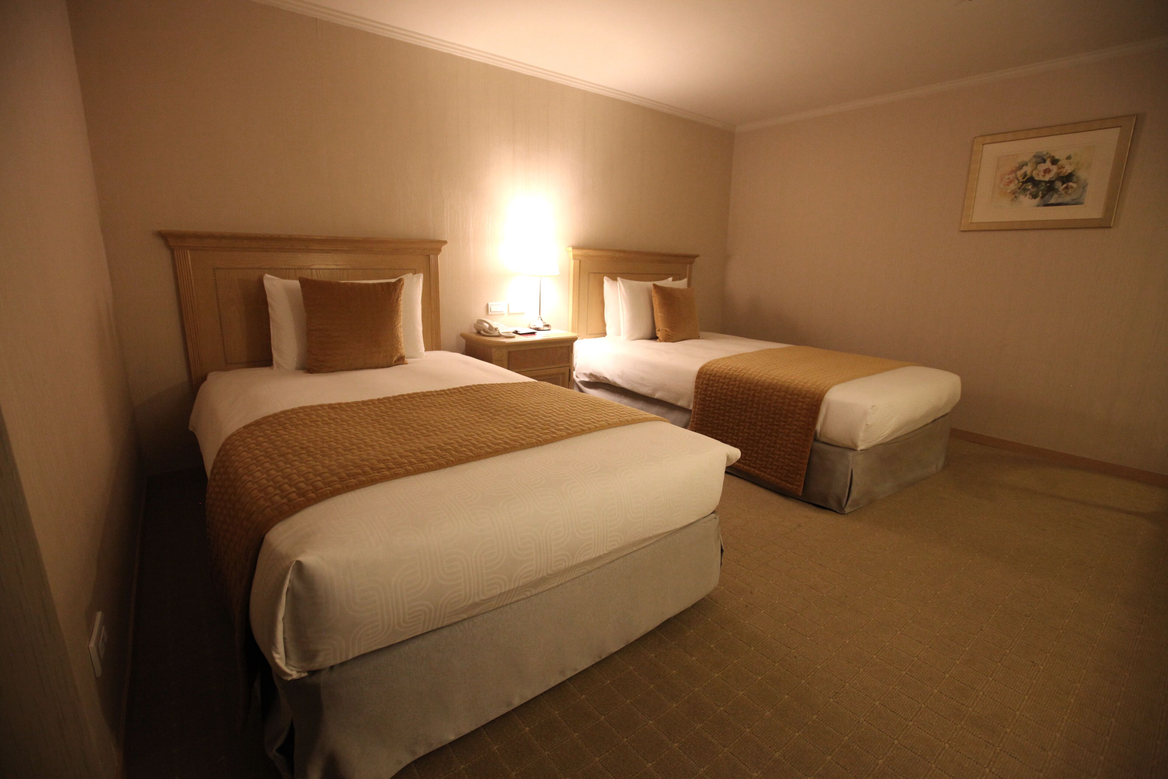 A hotel room with two beds, a nightstand with a lamp, and a framed picture on the wall.