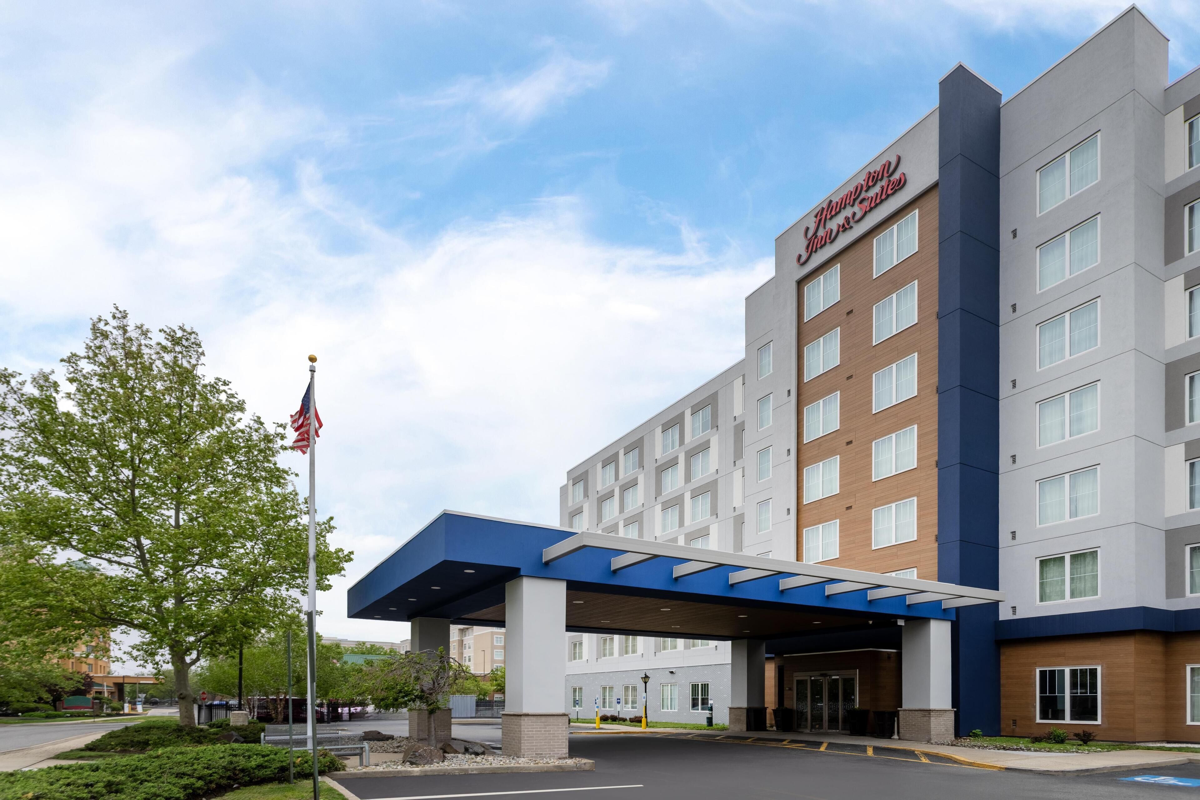 A modern hotel building with a prominent sign, a covered entrance, and a flagpole.