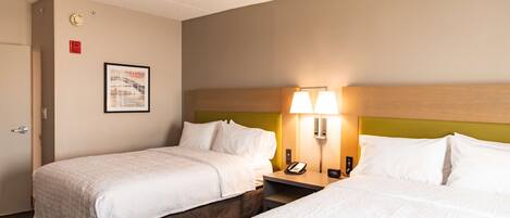 A hotel room with two beds, a nightstand with a lamp, a framed picture on the wall, and a clock.
