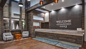 A modern reception area with a wooden reception desk, two armchairs, and a large wall-mounted screen.