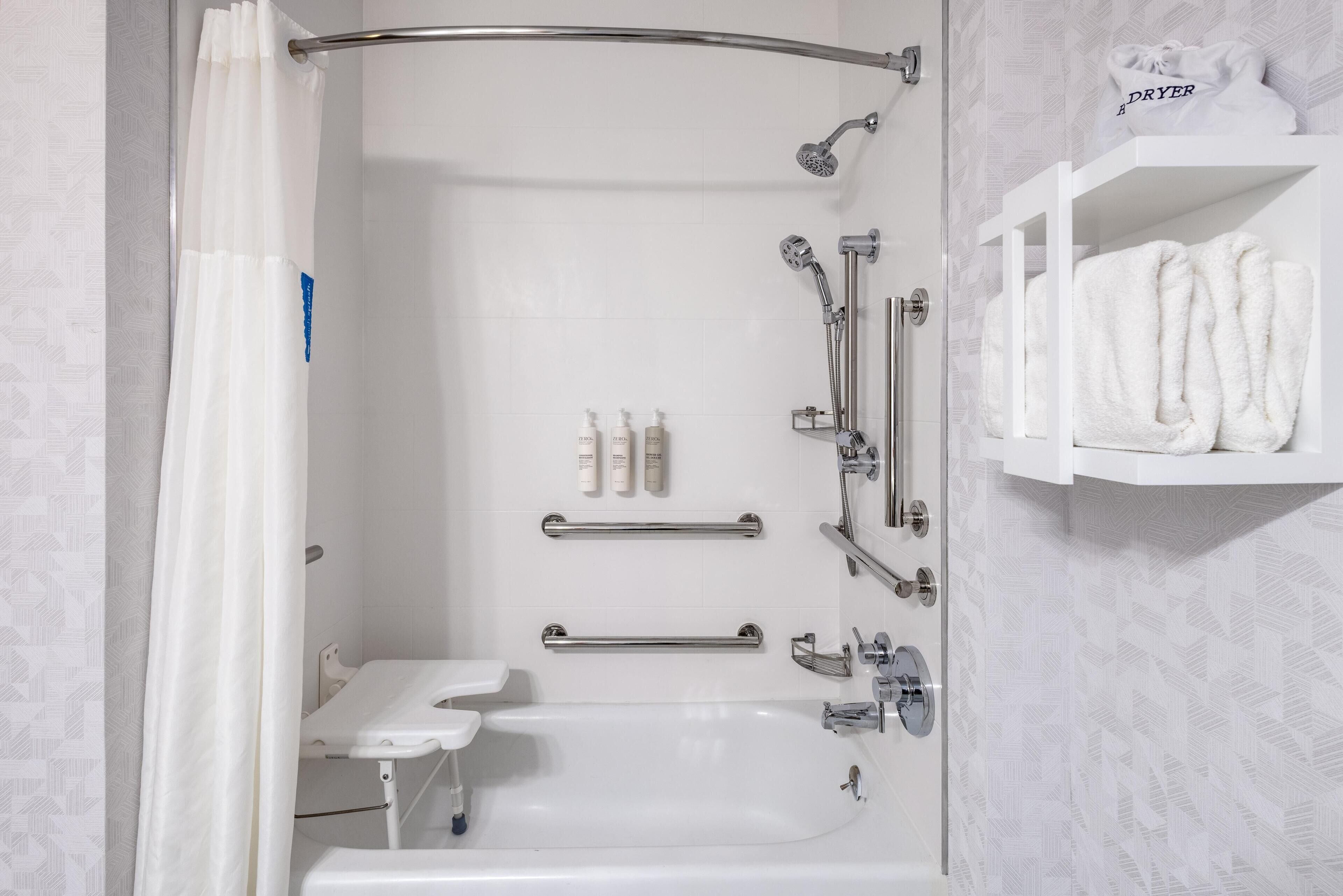 A modern bathroom with a shower, grab bar, and a shelf with towels.