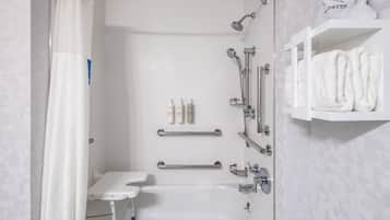 A modern bathroom with a shower, grab bar, and a shelf with towels.