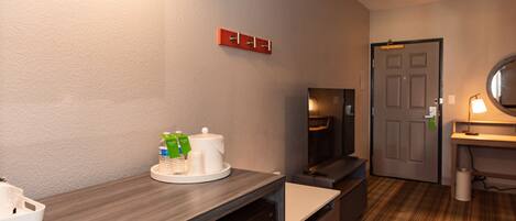 A hotel room with a wooden counter, a microwave, a television, and a door with a mirror.