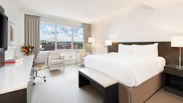 A hotel room with a large bed, a desk, a chair, a bench, and a TV.