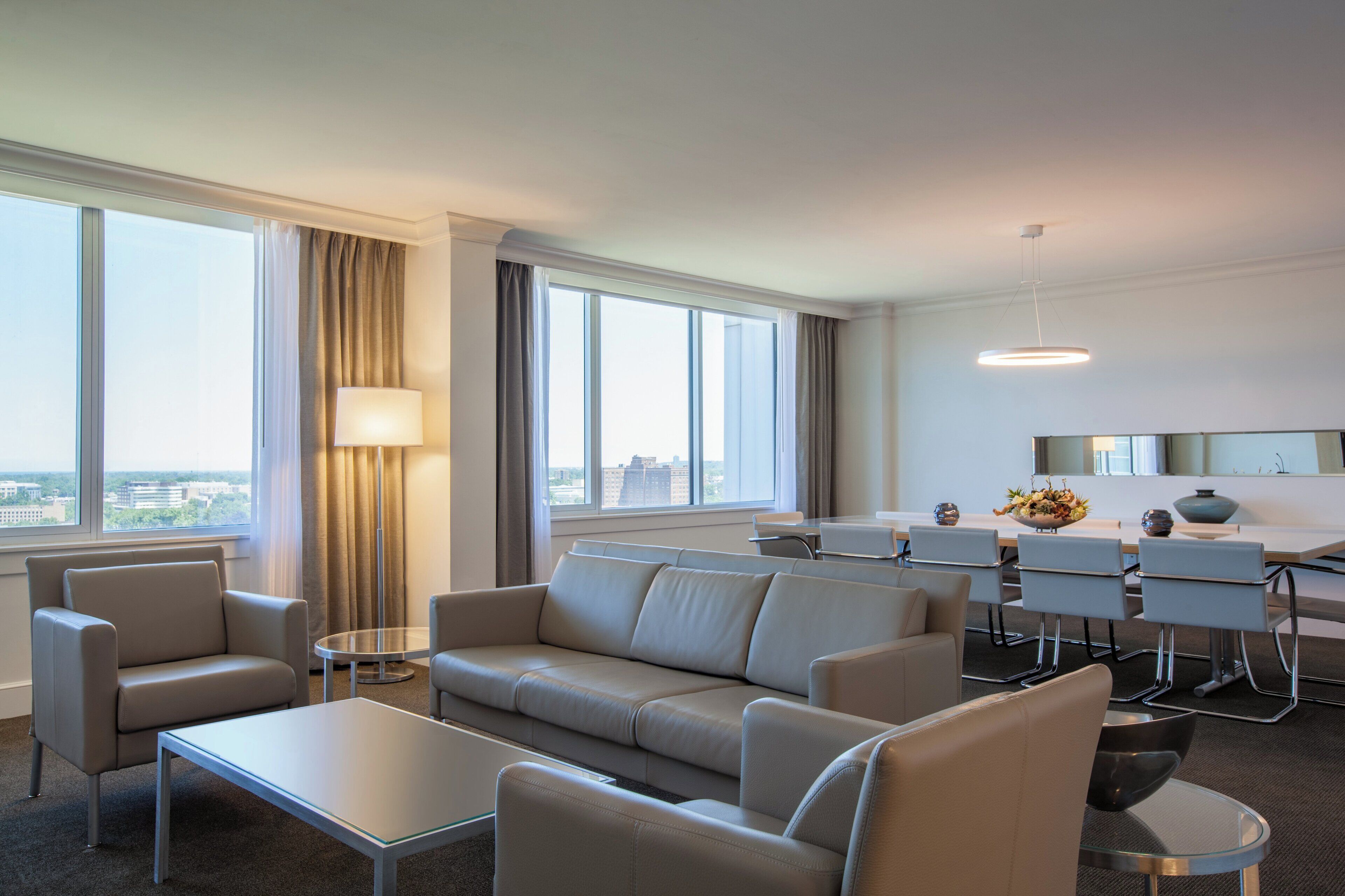 Et moderne hotelværelse med et siddeområde, et spisebord og store vinduer med udsigt over byen.