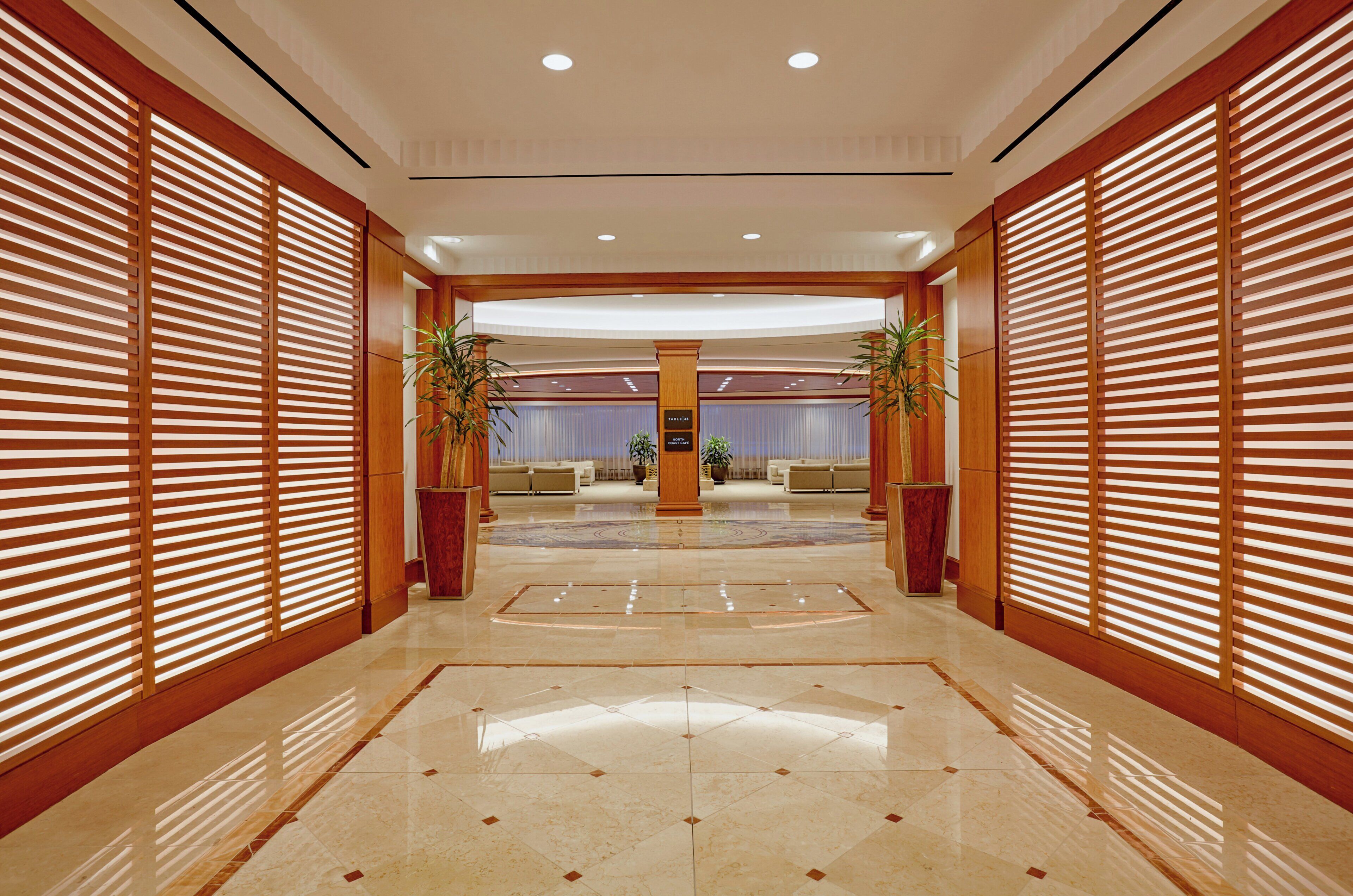 Un vestíbulo de hotel con un piso de mármol pulido, paneles de madera en las paredes y un mostrador de recepción en el centro.