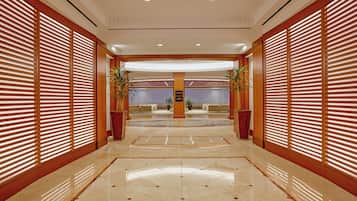 Un vestíbulo de hotel con un piso de mármol pulido, paneles de madera en las paredes y un mostrador de recepción en el centro.