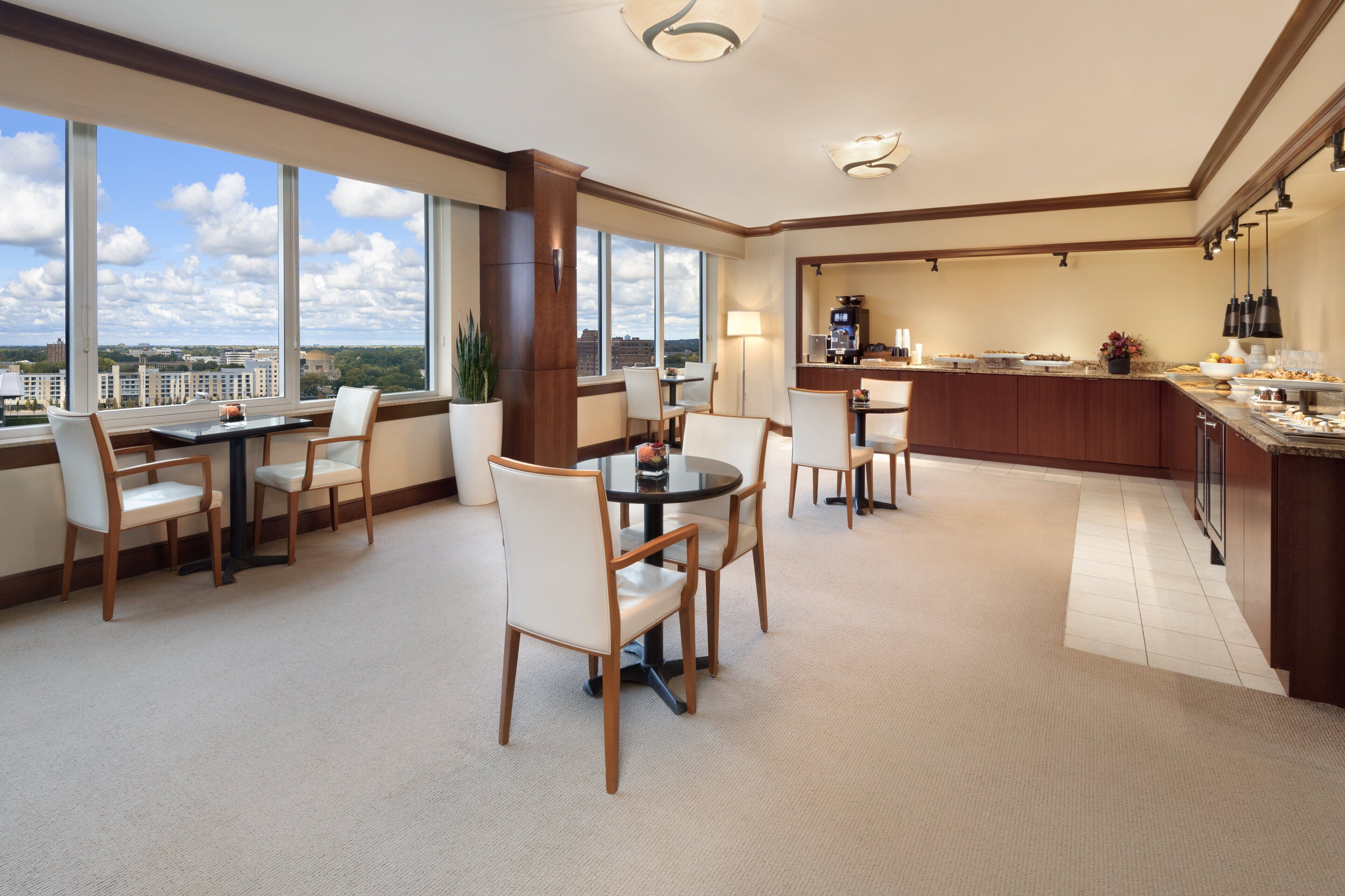A hotel room with a dining area, a kitchen, and large windows offering a city view.