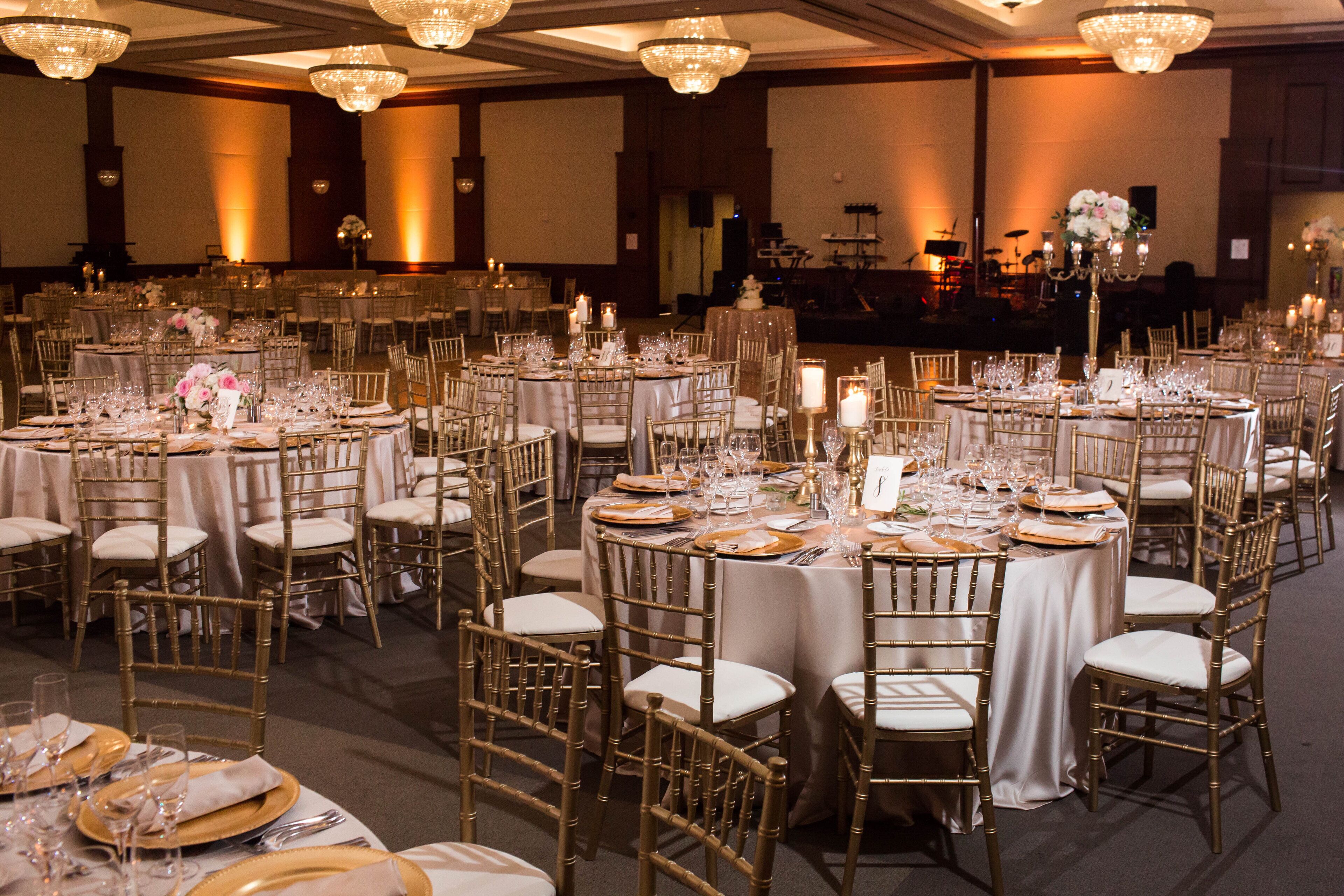 A banquet hall with round tables set for a formal event, featuring gold chairs and white tablecloths.