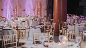 Een feestzaal met ronde tafels, stoelen en gedekte tafels voor een formeel evenement.