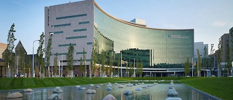 A modern building with a curved glass facade, a landscaped area with a pond and rocks, and a clear sky.