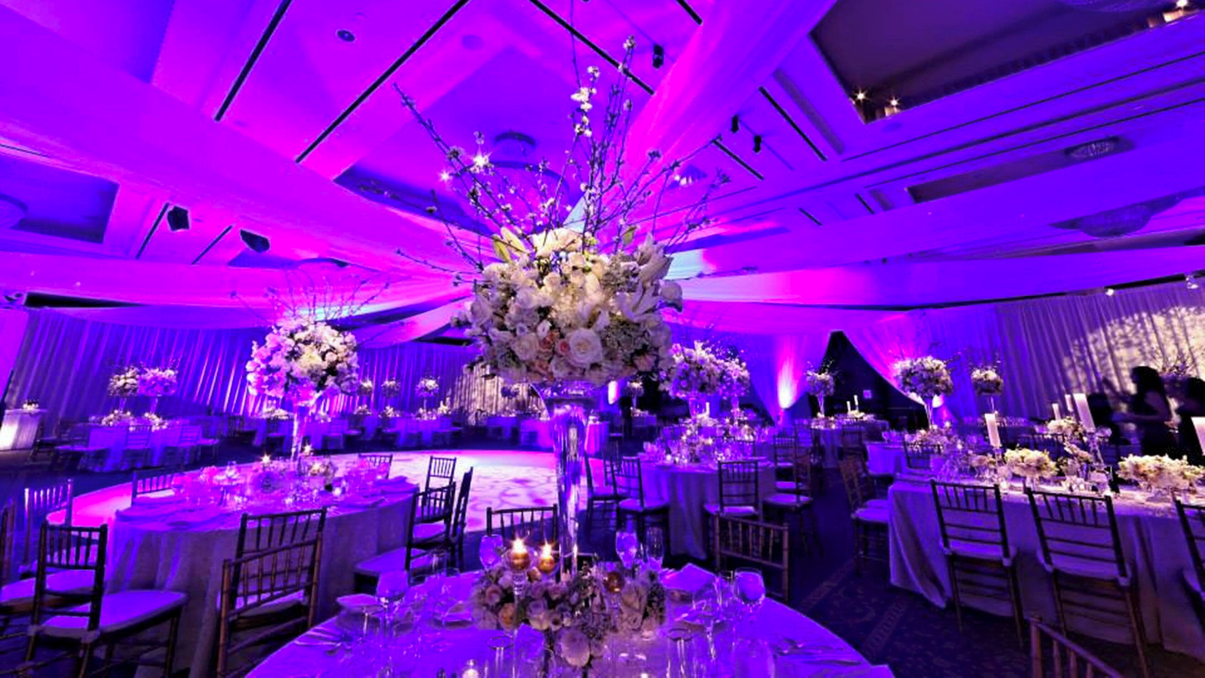 A banquet hall with round tables, chairs, and floral centerpieces.