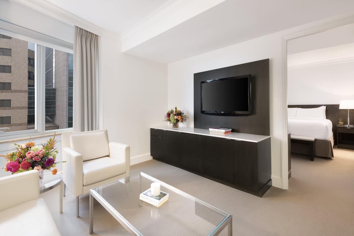 A modern hotel room with a flat-screen TV, a sofa, a coffee table, and a bed.