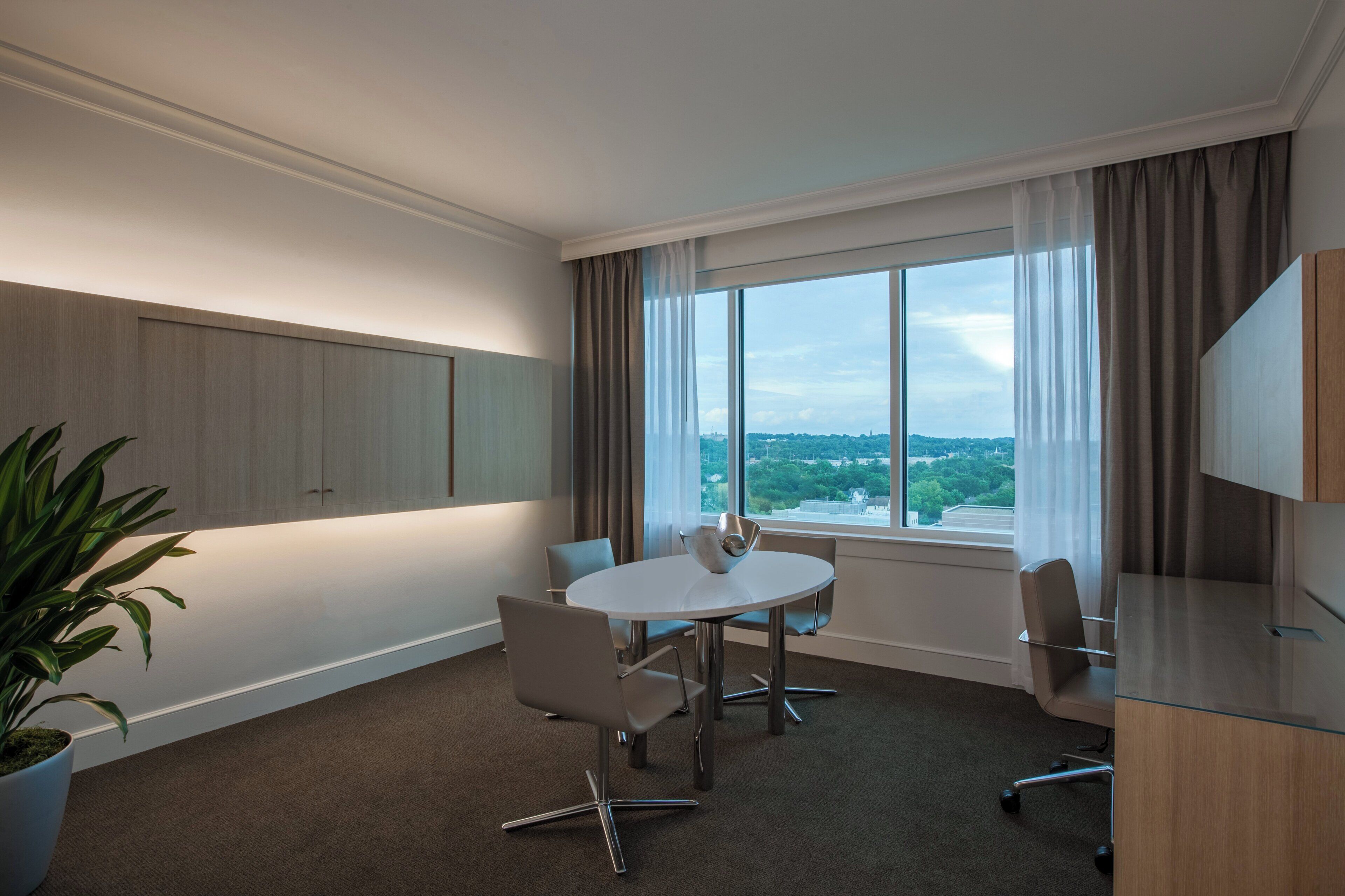 A conference room with a large window, a white table, and four chairs.