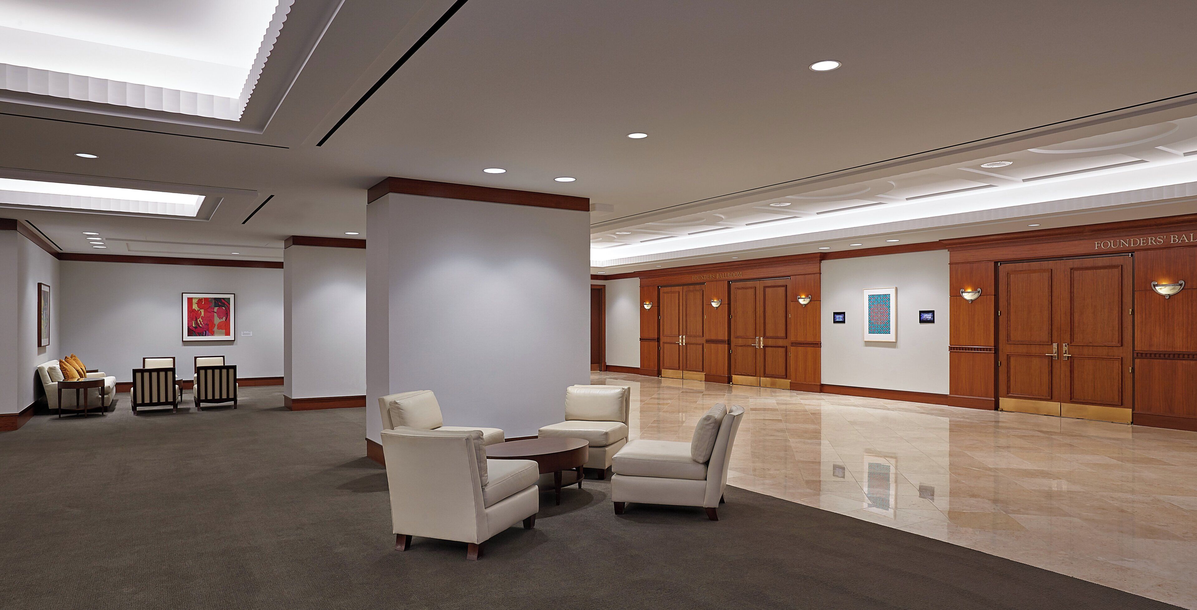 A spacious lobby with a high ceiling, recessed lighting, and a polished marble floor. There are seating arrangements and a wall-mounted art piece.