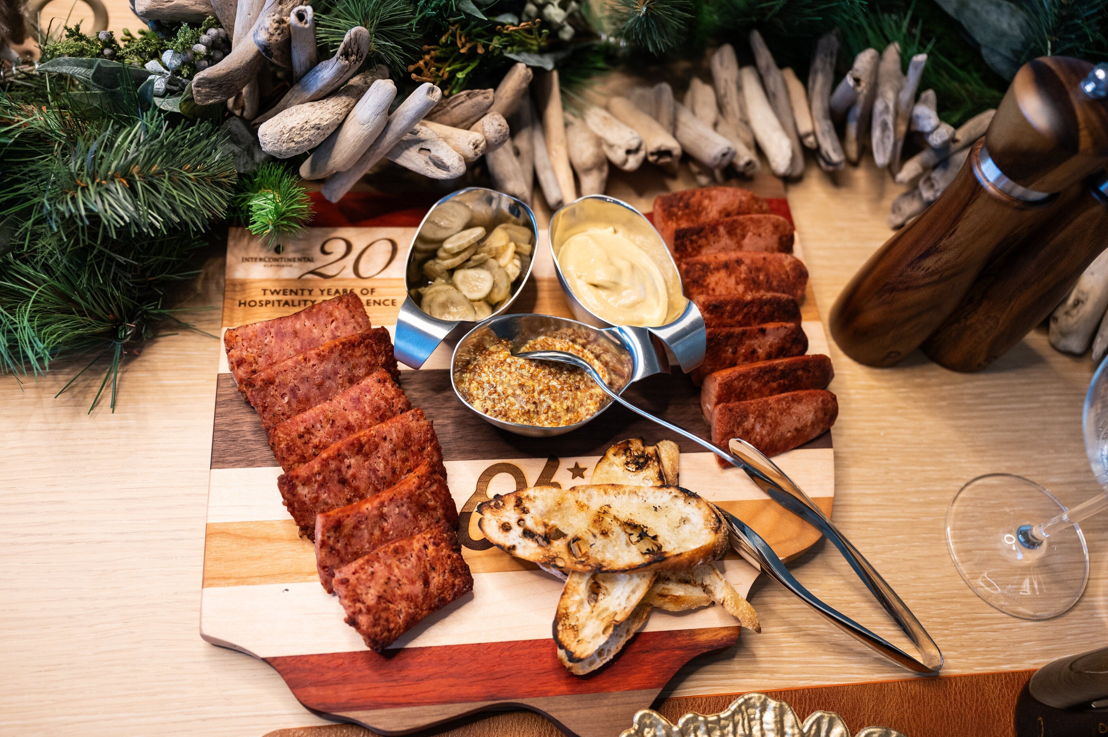 Une planche de charcuterie comprenant différentes sortes de viandes, de fromages et de condiments, accompagnée d’un verre de vin et d’un moulin à poivre en bois.