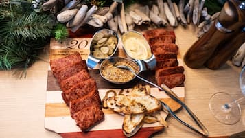 Une planche de charcuterie comprenant différentes sortes de viandes, de fromages et de condiments, accompagnée d’un verre de vin et d’un moulin à poivre en bois.