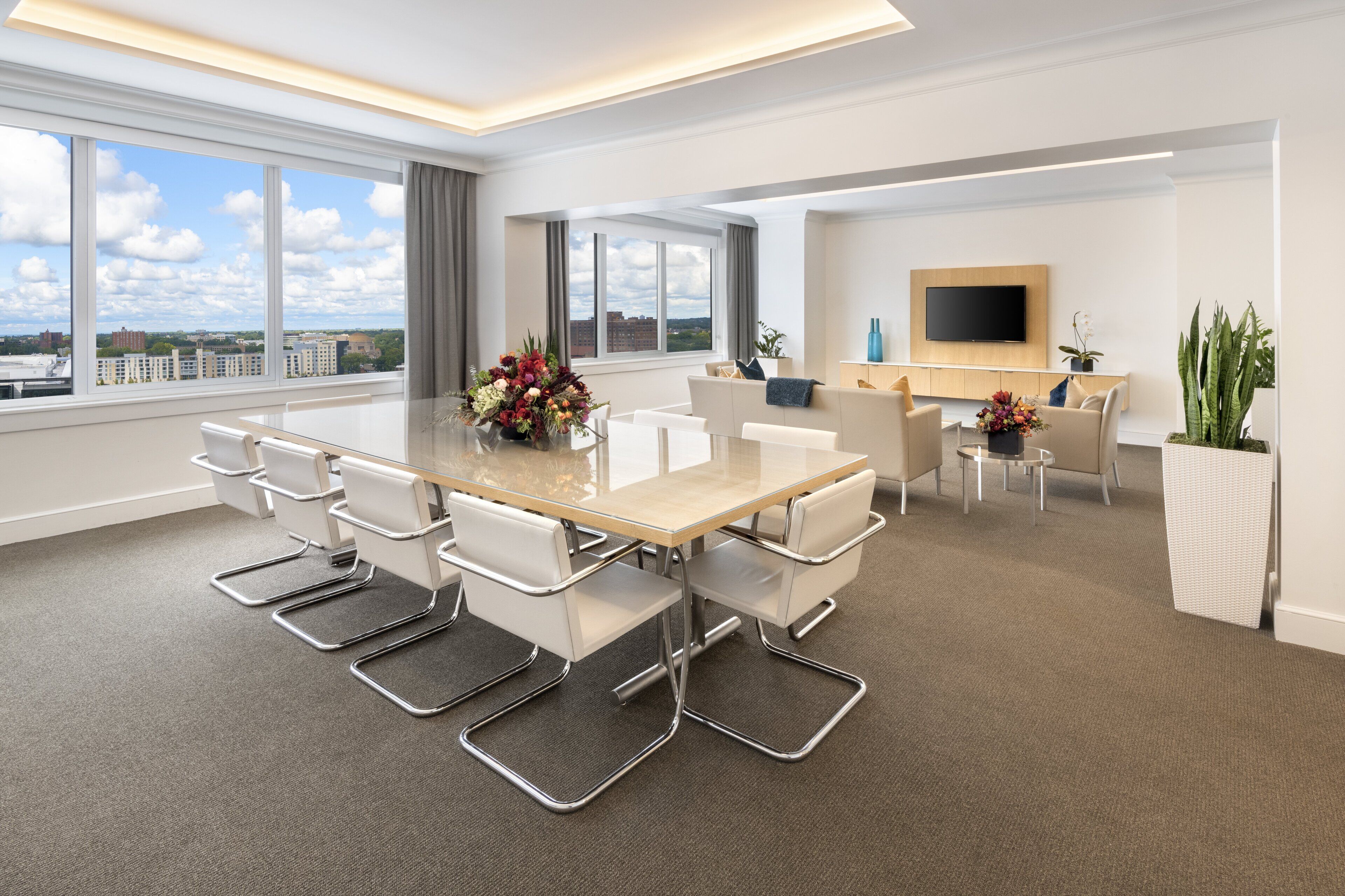 Una sala de conferencias moderna con una gran mesa, sillas blancas y vistas a la ciudad.