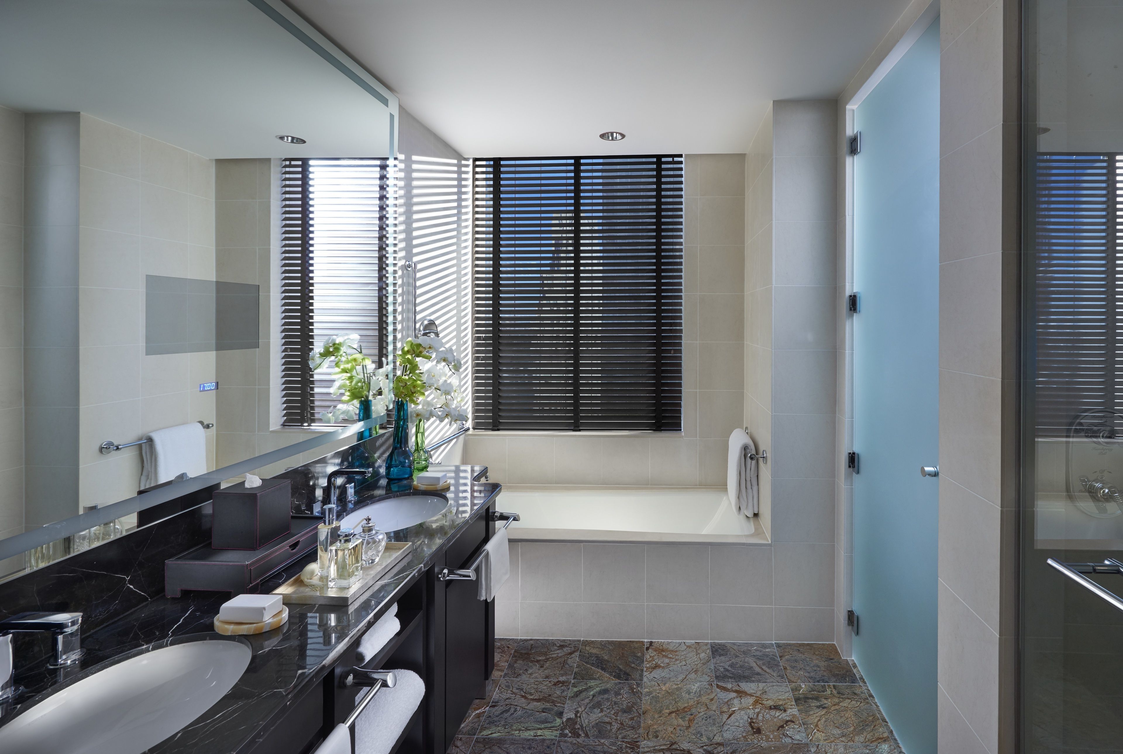 A modern bathroom with a large mirror, two sinks, a bathtub, and a shower.