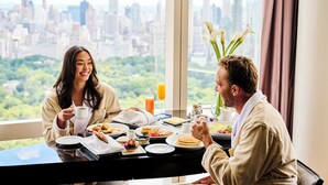 A breakfast setting with a city view, including a table with plates of food, a coffee cup, and a vase with flowers. - Mandarin Oriental, New York (New York)