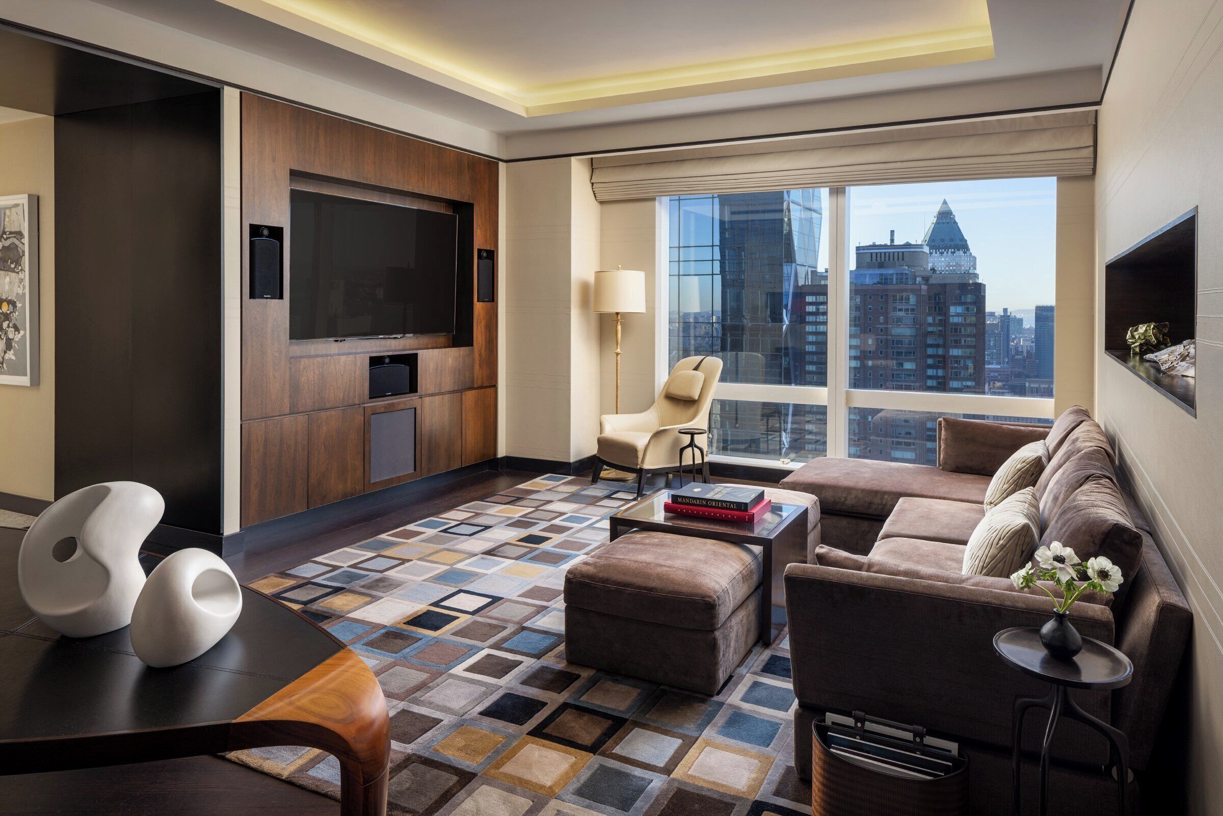 Quarto de hotel moderno com televisão de tela grande, um sofá, uma poltrona e uma mesa de centro.
