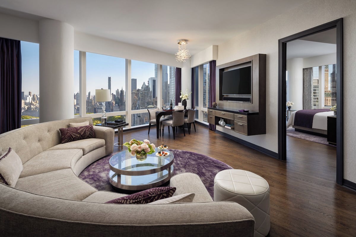 Een moderne hotelkamer met een ruime bank, een eethoek, een televisie en uitzicht over de stad.