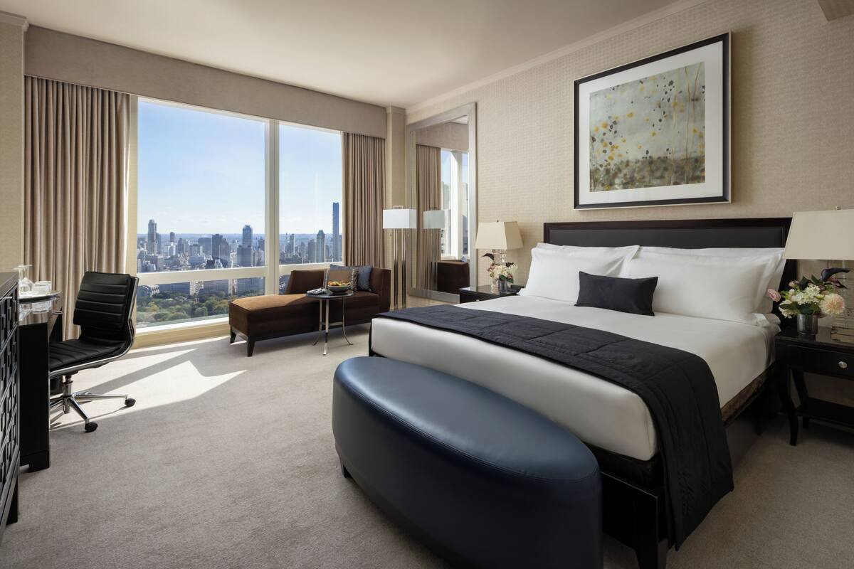 A hotel room with a large bed, a desk, a chair, a sofa, and a view of the city.