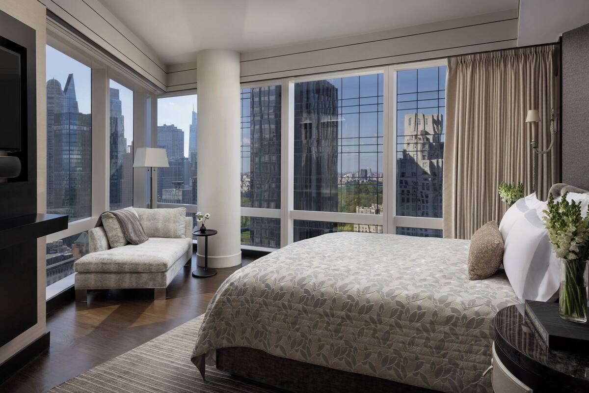 Een moderne hotelkamer met een groot bed, een sofa en een televisie. De kamer heeft grote ramen met uitzicht op de stad.