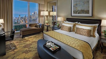 A hotel room with a large bed, a sofa, a desk, and a view of a cityscape.
