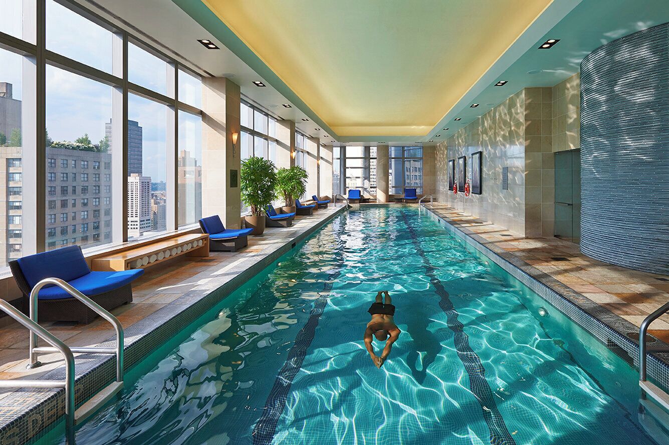 An indoor swimming pool with clear blue water, surrounded by lounge chairs and potted plants.