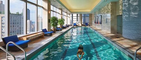 Una piscina interior con agua cristalina, rodeada de sillones de descanso y plantas en macetas.