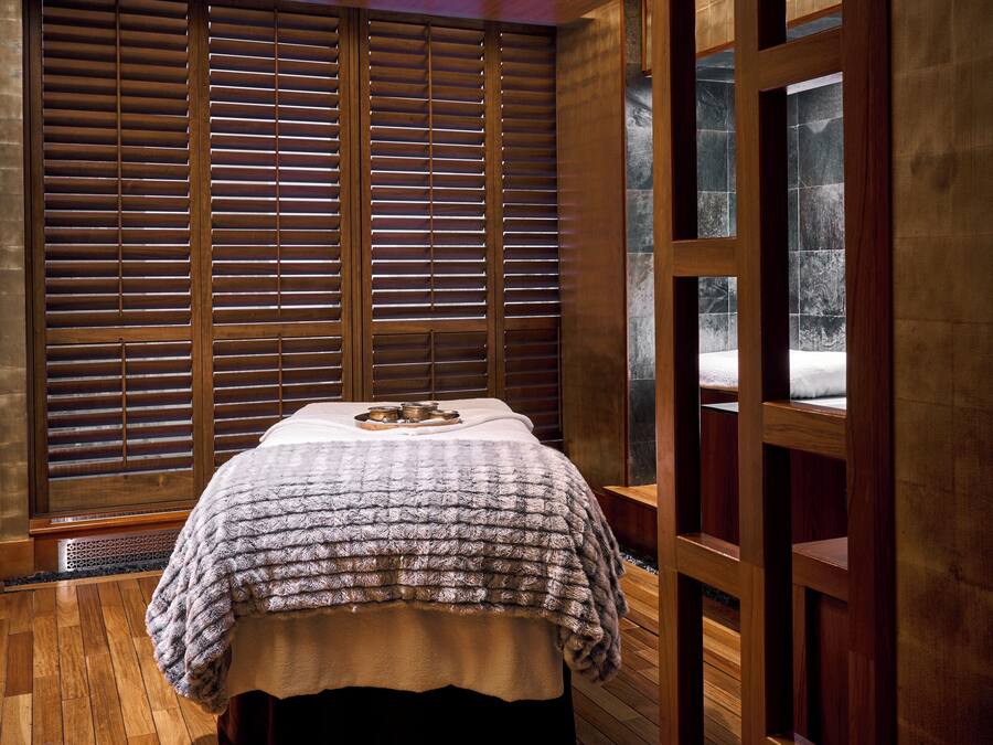 Une chambre avec un plancher en bois, un lit recouvert d’une couvre-lit à motifs, des portes coulissantes en bois et une vue à travers ces portes.