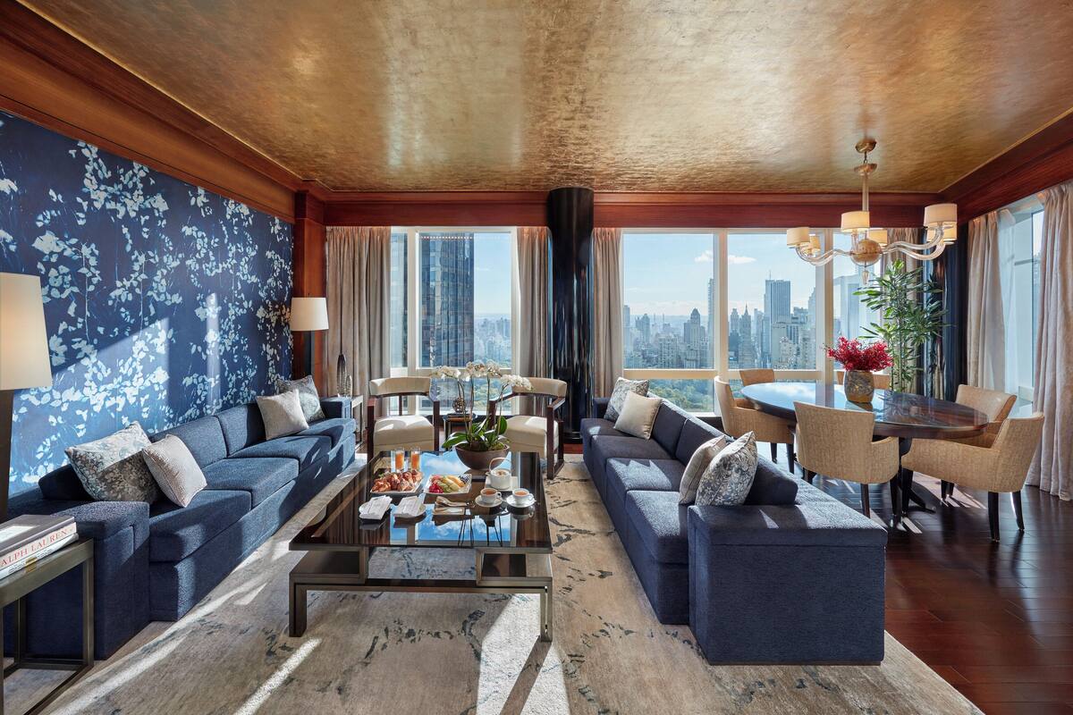 A modern living room with a city view, a large sofa set, a dining table, and a coffee table with decorative items.