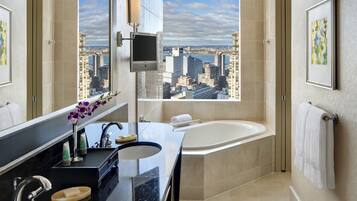 Un baño moderno con una bañera grande, un tocador con espejo y un ventanal con vistas a la ciudad.