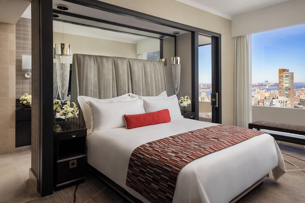 Een moderne hotelkamer met een groot bed, nachtkastje, spiegel en stadszicht.