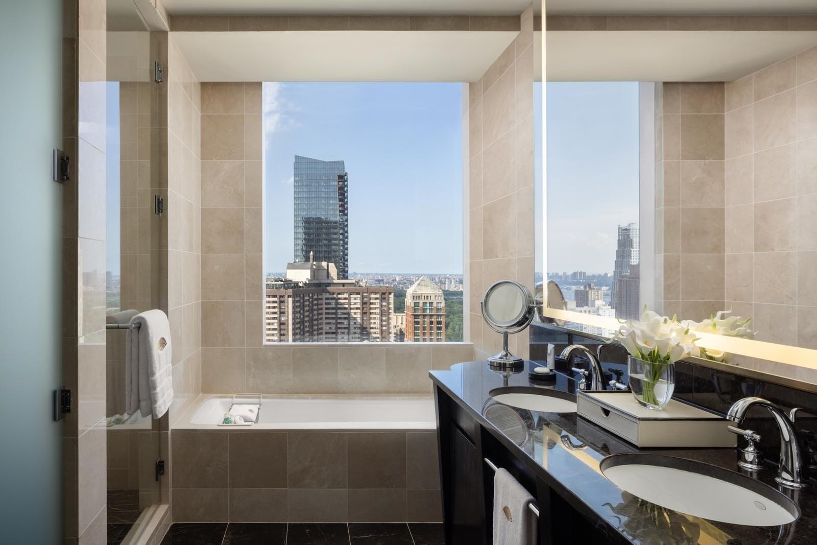 Ein modernes Badezimmer mit einer Badewanne, zwei Waschbecken, einem Spiegel und Blick auf die Stadt.