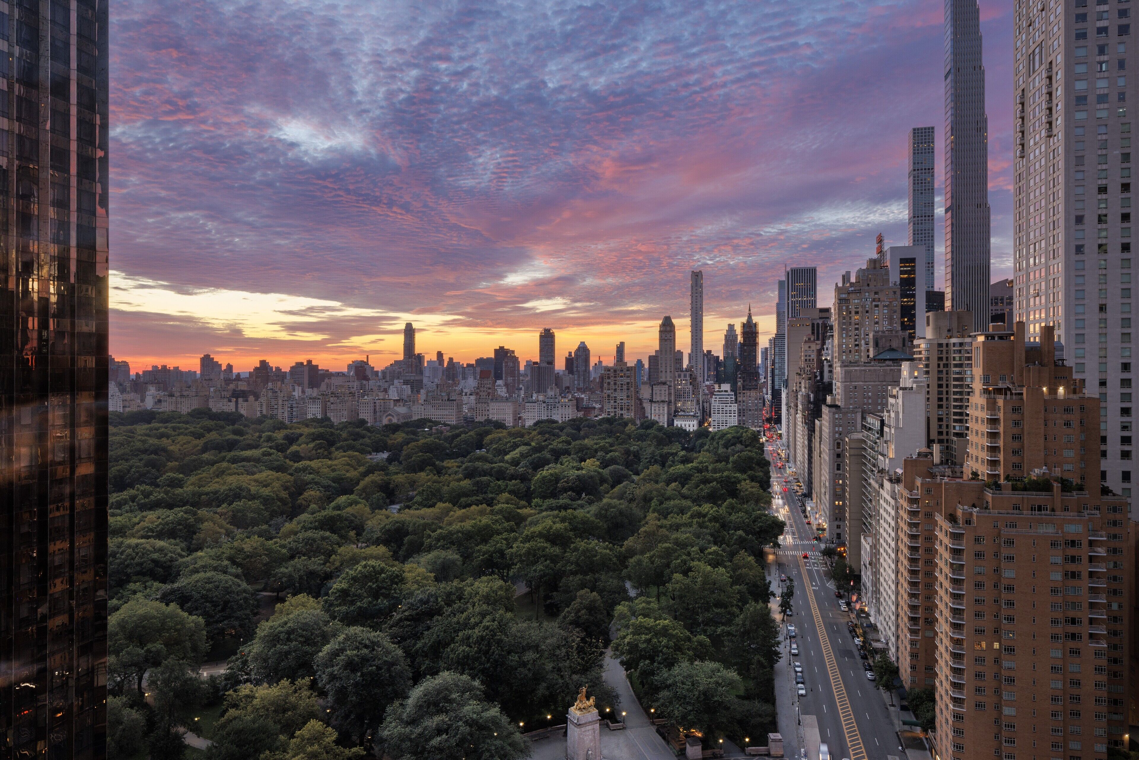 A cityscape with a dense urban area, a park with trees, and a sunset sky.