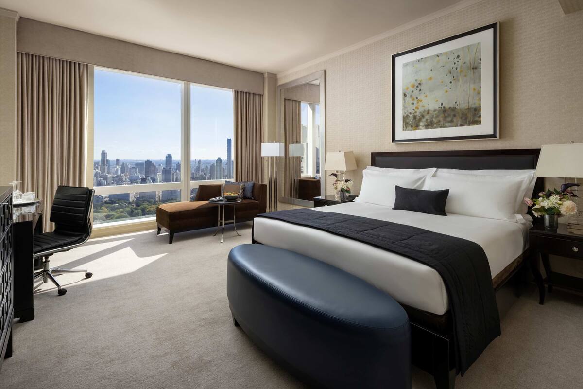 Een hotelkamer met een groot bed, een bureau, een stoel en uitzicht op de stad.