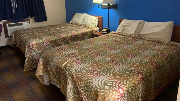 Habitación de hotel con dos camas, una mesita de noche, una lámpara y una ventana con cortinas.
