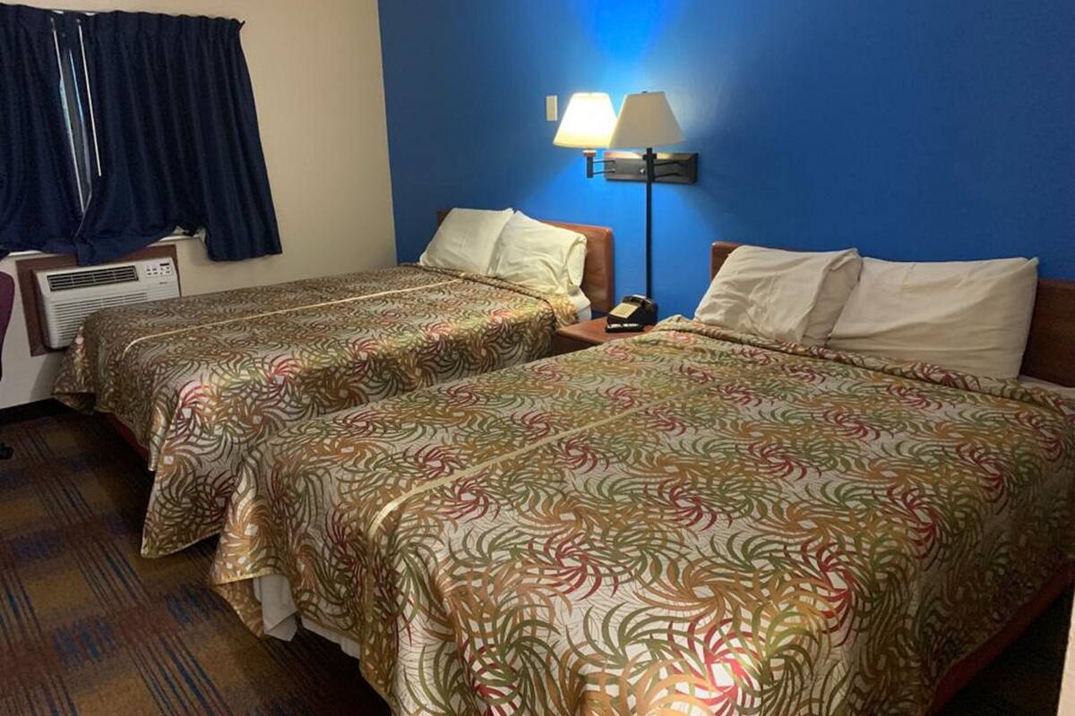 A hotel room with two beds, a nightstand, a lamp, and a window with curtains.