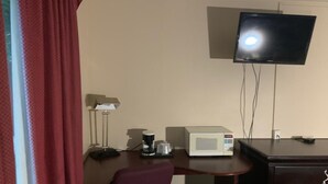 Una habitación de hotel con escritorio, televisor montado en la pared, cafetera y microondas.
