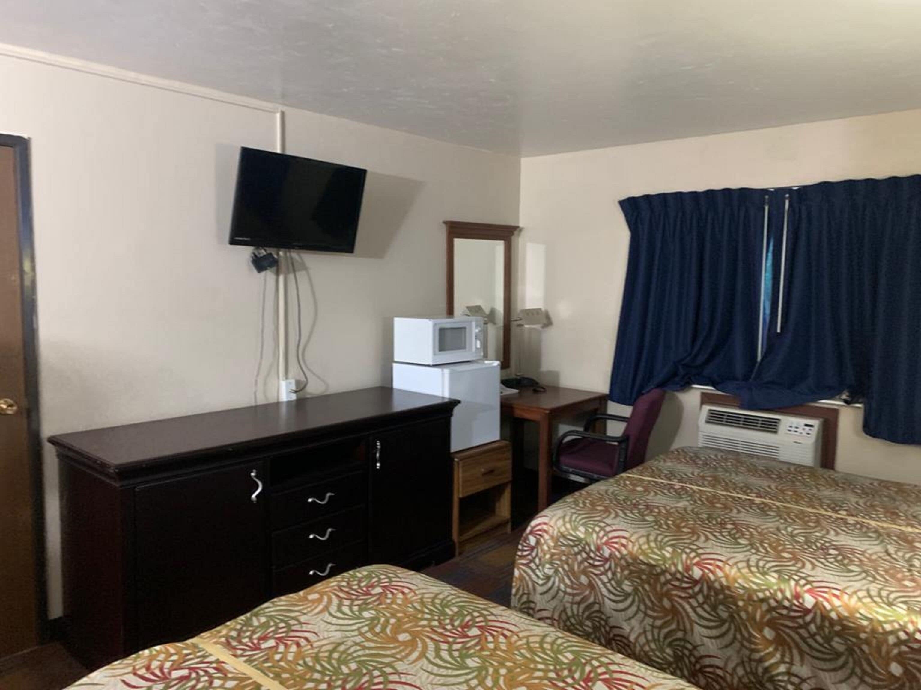 Une chambre d’hôtel équipée d’un lit, d’un bureau, d’une télévision, d’un four à micro-ondes et d’une fenêtre avec des rideaux.