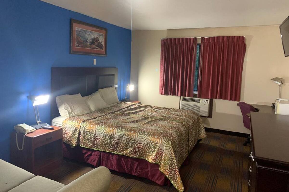 A hotel room with a bed, a desk, a chair, a nightstand, and a window with curtains.